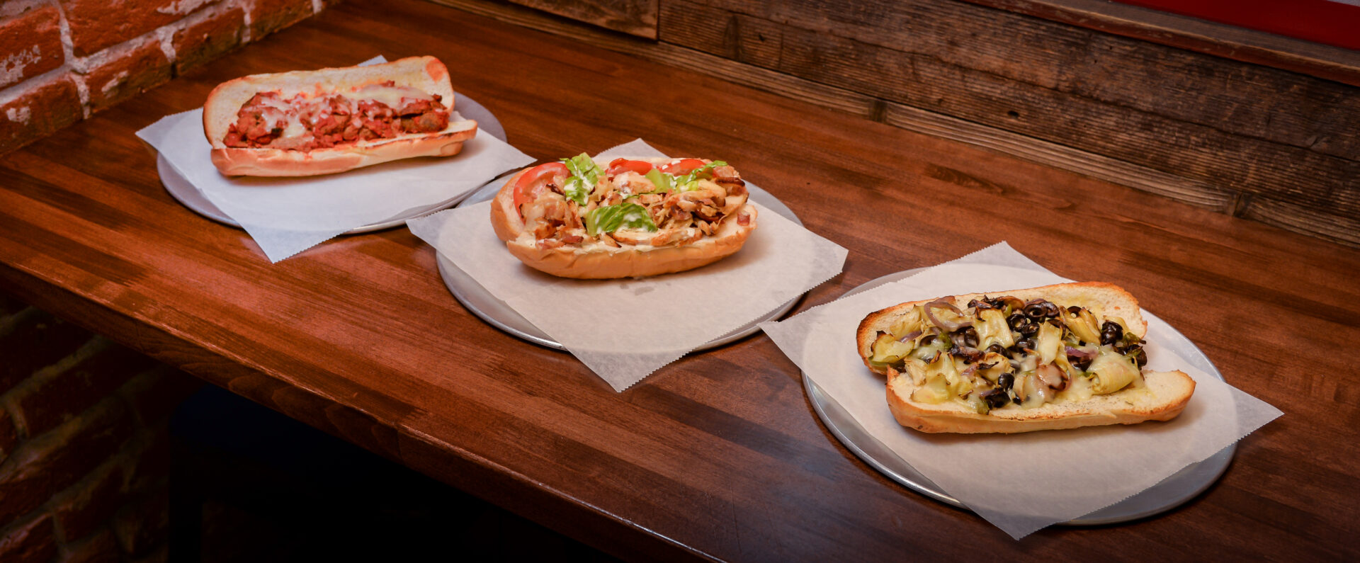 A wooden table with three sandwiches on it.