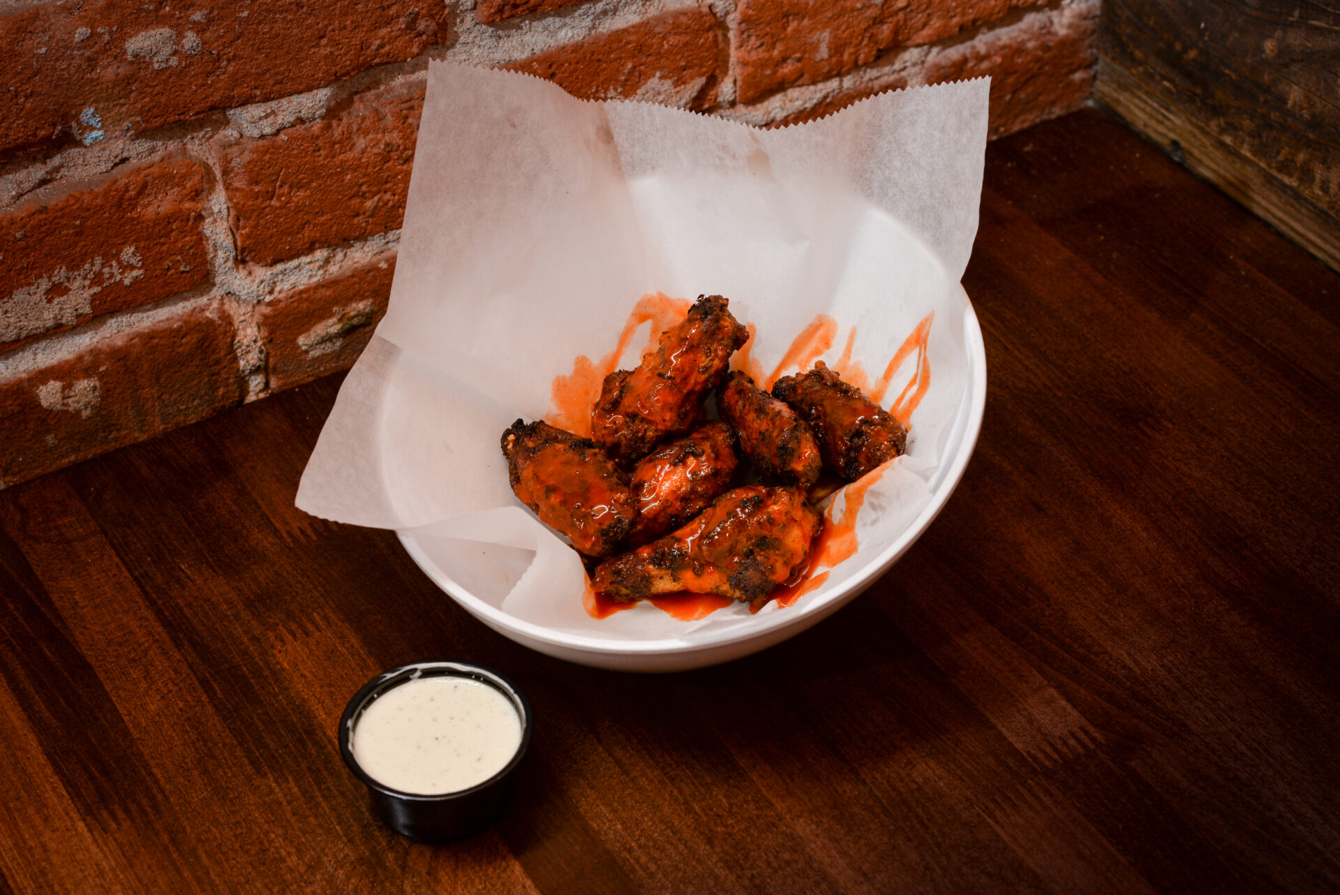 A bowl of chicken wings next to a cup of sauce.